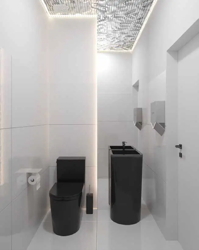 Grup sanitar alb cu vas de toaletă și lavoare negre, două uscătoare de mâini din inox și tavan metalic ondulat.