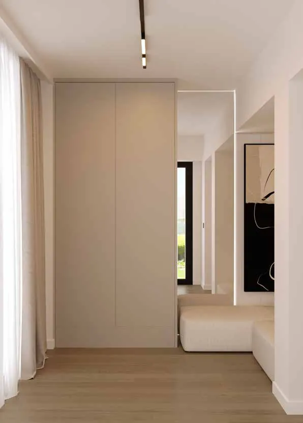 Dulap bej fără mânere lângă draperii, oglindă înaltă cu margine luminată, tablou alb-negru și un șezut tapițat crem.